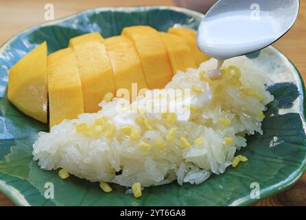 Ajouter du lait de coco crémeux sur du riz collant Chewy servi avec de la mangue mûre fraîche et juteuse Banque D'Images