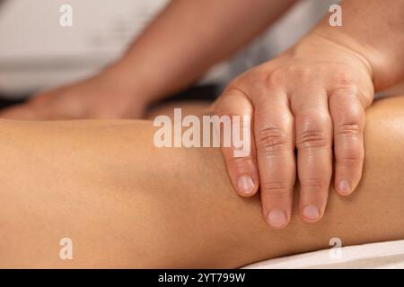 Gros plan des mains du massothérapeute travaillant sur la jambe du patient, apportant un soulagement et favorisant la relaxation Banque D'Images