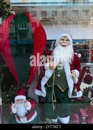 Cette photo de jour capture une vitrine festive mettant en vedette deux personnages du Père Noël vêtus d'une tenue rouge et verte classique. Un Père Noël se tient uprig Banque D'Images