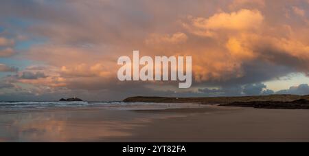 Un panorama de la plage de Gwithian et du phare de Godrevy avec de superbes nuages de coucher de soleil orange reflétés dans une étendue de sable humide Banque D'Images