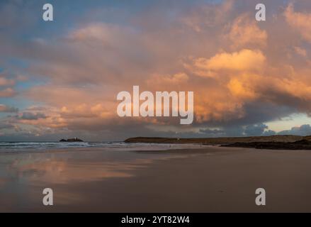 Gwithian Beach et Godrevy Lighthouse avec de superbes nuages de coucher de soleil orange reflétés dans une étendue de sable humide Banque D'Images