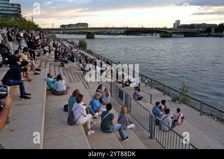 Allemagne, Rhénanie du Nord-Westphalie, Cologne, promenade du Rhin, jeunes assis sur les marches, soirée, coucher de soleil Banque D'Images