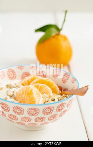 Petit déjeuner muesli avec flocons d'avoine, yaourt et mandarines dans un bol avec une cuillère Banque D'Images