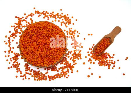 Un bol en osier rempli de lentilles rouges, accompagné d’une cuillère en bois, entouré de grains de lentilles rouges. Banque D'Images