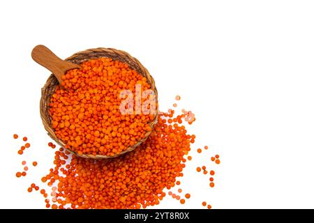 Un bol en osier rempli de lentilles rouges, contenant une cuillère en bois et entouré de grains de lentilles rouges dispersés. Banque D'Images