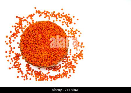 Un bol en osier rempli de lentilles rouges, entouré de grains de lentilles rouges dispersés. Banque D'Images