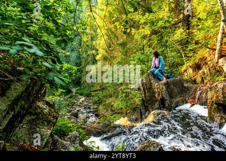 une femme est assise sur un rocher au bord d'une cascade et regarde vers le bas Banque D'Images