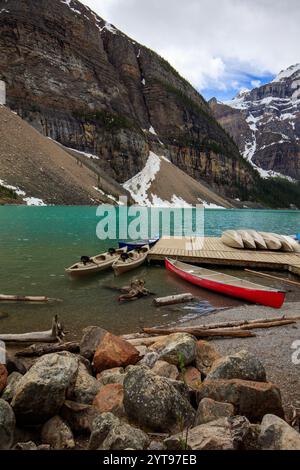 Un groupe de canoës est amarré à un lac, avec une montagne en arrière-plan. La scène est paisible et sereine, avec l'eau reflétant le ciel et le Banque D'Images