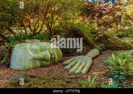 Une grande statue représentant la tête d'un homme et une main est posée sur le sol dans un jardin. La statue est faite de pierre et il est une représentation de fa d'une personne Banque D'Images