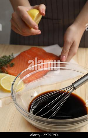 Femme pressant le jus de citron sur le filet de saumon en bois à table, concentrez-vous sur le bol avec la sauce soja Banque D'Images