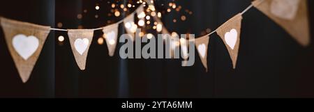 Chaîne de fête extérieure suspendue dans un style boho avec des coeurs et des lumières dorées au ciel nocturne. Fond horizontal de partie d'été avec une courte profondeur de champ pour mariage et vacances. Banque D'Images