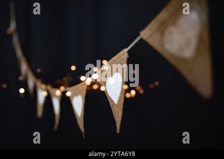 Chaîne de fête extérieure suspendue dans un style boho avec des coeurs et des lumières dorées au ciel nocturne. Fond de partie d'été avec une courte profondeur de champ pour mariage et vacances. Banque D'Images