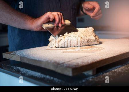 Mains pliant et pétrissant la pâte à pain sur une surface de travail en bois avec de la farine. Gros plan. Fond pour l'artisanat de boulangerie. Banque D'Images