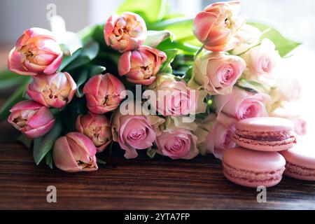 Beau bouquet rose de fleurs et délices sur bois sombre. Pâtisseries sucrées aux roses et tulipes. Fond de concept pour les célébrations de mariage et la fête des mères. Banque D'Images