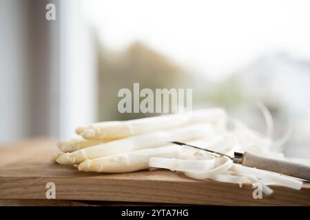 Asperges blanches fraîchement pelées sur planche à découper en bois. Scène de cuisine lumineuse avec des légumes de printemps pour la gastronomie saisonnière. Faible profondeur de champ. Banque D'Images