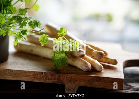 Asperges blanches fraîches et persil sur planche à découper en bois. Légumes de printemps de saison avec persil. Scène de cuisine pour la gastronomie saisonnière. Banque D'Images