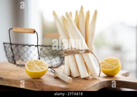 Bouquet debout d'asperges blanches fraîches. Légumes de printemps de saison avec citron sur planche à découper en bois. Scène de cuisine pour la gastronomie saisonnière. Banque D'Images