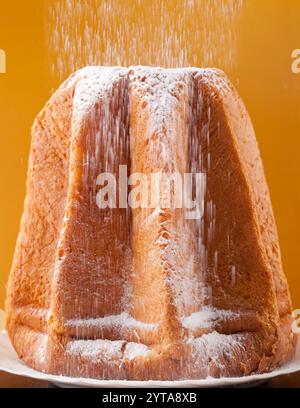 Avec Pandoro saupoudrage de sucre glace sur fond orange Banque D'Images