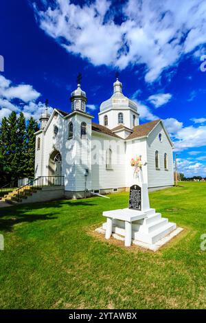 Une église blanche avec une croix sur un piédestal blanc. L'église est entourée d'une zone herbeuse verte Banque D'Images