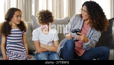 Amusement, jeu et rire avec la famille sur le canapé dans le salon de la maison ensemble pour la compétition. Fille, fils contrariés et mère gagnante jouant au jeu vidéo Banque D'Images