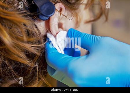 esthéticienne en gants bleus marque l'endroit où les oreilles seront percées. Style et beauté Banque D'Images