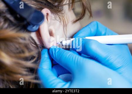 esthéticienne en gants bleus marque l'endroit où les oreilles seront percées. Style et beauté Banque D'Images