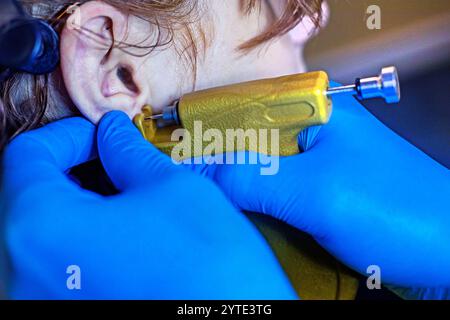 esthéticienne en gants bleus crée un trou dans les oreilles avec un outil spécial. Perçage d'oreilles style et beauté Banque D'Images