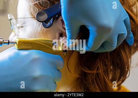 esthéticienne en gants bleus crée un trou dans les oreilles avec un outil spécial. Perçage d'oreilles style et beauté Banque D'Images