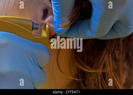 cosmétologue en gants bleus perce des trous dans les oreilles avec un pistolet. Style et beauté Banque D'Images