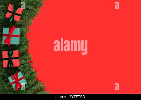 Bordure de Noël avec des branches de sapin et des boîtes-cadeaux sur un fond rouge avec espace de copie. Carte de Noël ou de nouvel an. Vue de dessus. Banque D'Images