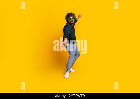 Jeune homme énergique dans des lunettes de soleil vert vif pose sur fond jaune vif Banque D'Images