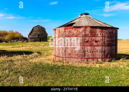 Une grange rouge avec un tonneau rouge sur l'herbe. La grange est vieille et le tonneau rouillé Banque D'Images