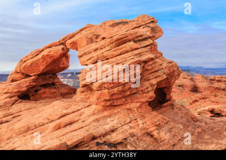 Une grande formation rocheuse avec un trou au milieu. La roche est orange et a beaucoup de texture. Le ciel est bleu et il y a quelques nuages dans le backgr Banque D'Images