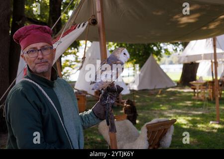 Mantova, Italie - 15 septembre 2024 : un fauconnier en costume médiéval tient doucement un hibou blanc de grange lors d'une reconstitution historique en plein air. Banque D'Images