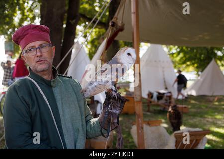 Mantova, Italie - 15 septembre 2024 : un fauconnier en costume médiéval tient doucement un hibou blanc de grange lors d'une reconstitution historique en plein air. Banque D'Images