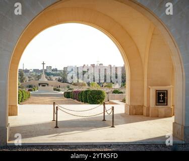 Une vue paisible sur le cimetière de guerre d'El Alamein (britannique), encadré par une arche en pierre, mettant en évidence la croix commémorative de la seconde Guerre mondiale et les jardins en Égypte. Banque D'Images