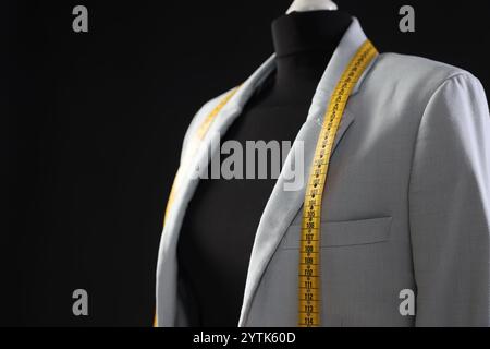 Mannequin femme avec veste grise et ruban à mesurer sur fond noir, gros plan. Espace pour le texte Banque D'Images