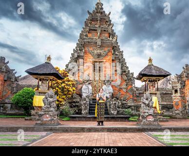 Une jeune touriste vêtue de vêtements traditionnels balinais prie avec ses mains ensemble devant un temple à Bali, en Indonésie, avec une dramatique Banque D'Images