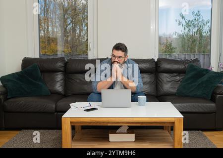 Un homme stressé avec une pensée profondément inquiète tout en travaillant sur un ordinateur portable à la maison. Banque D'Images