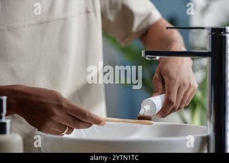 Plan recadré de Black Man appliquant soigneusement du dentifrice sur la brosse à dents en bambou en prenant soin de la santé bucco-dentaire dans la salle de bain avec zéro produit de déchet, espace de copie Banque D'Images