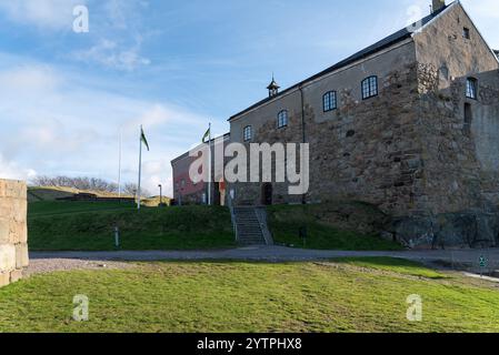 Une forteresse en pierre robuste se dresse bien en évidence au sommet d'une colline, entourée d'une herbe verte luxuriante et d'un ciel bleu clair. Les drapeaux flottent dans la douce brise, haut Banque D'Images