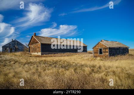 Une petite maison ancienne se trouve dans un champ avec un ciel nuageux en arrière-plan. La maison est entourée d'un champ sec et poussiéreux sans arbres en vue. La scène est Banque D'Images