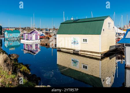 Une rangée de maisons colorées se trouve sur l'eau, l'une d'elles étant une grande maison blanche avec un toit vert. L'eau est calme et le ciel dégagé, créat Banque D'Images