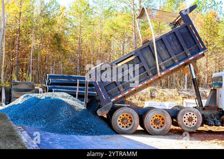 Le camion à benne basculante relâche une grosse pile de gravier sur le sol sur un chantier de construction très fréquenté. Banque D'Images