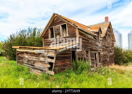 Une vieille maison délabrée avec une grande grange en arrière-plan. La maison est dans un cadre rural avec beaucoup d'herbe et d'arbres Banque D'Images