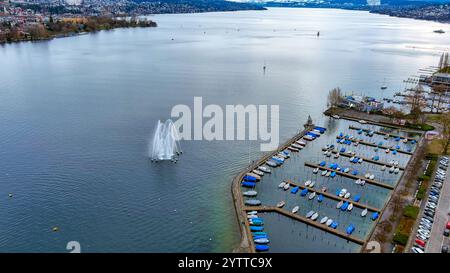 Une vue aérienne sereine du lac de Zurich avec une fontaine pittoresque et un port de plaisance remplis de bateaux animés, entourés de paysages tranquilles. Banque D'Images