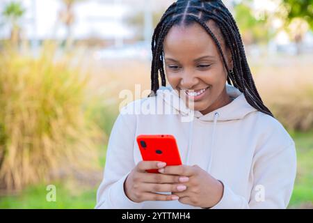 Jeune femme souriante tenant un smartphone à l'extérieur dans une tenue décontractée Banque D'Images