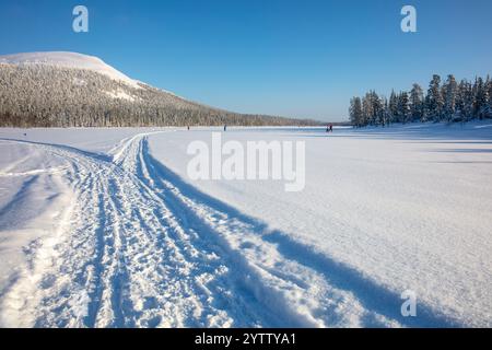 Laponie finlandaise en hiver. Journée ensoleillée et ciel bleu sur la montagne enneigée et la forêt. Large piste de ski sur le lac gelé Banque D'Images