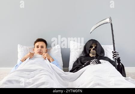 Homme effrayé couché dans son lit à côté de Grim Reaper Banque D'Images