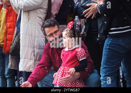 L'image représente un homme et une jeune fille. L'homme est assis et a des lunettes et des poils sur le visage. Il porte une chemise rouge et un Jean bleu. Il regarde Banque D'Images